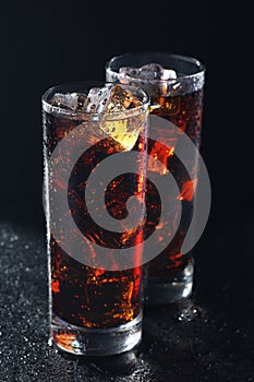 Glasses of cola with ice cubes on black stone