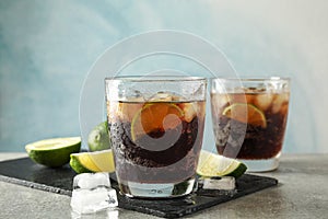 Glasses with cold cola and citrus on grey table