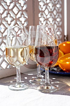 Glasses with cold dry fino and sweet cream sherry fortified wine and orange in sunlights, andalusian style interior on background