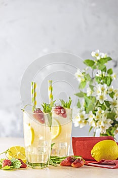 Glasses of cold icy refreshing drink with lemon and strawberry served on light pink table. Fresh cocktail drinks with ice fruit