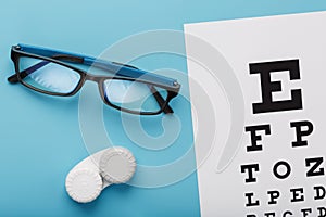 Glasses with Contact Lenses, drops and an Optometrist`s Eye Test Chart On a Blue Background