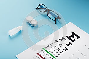 Glasses with Contact Lenses, drops and an Optometrist`s Eye Test Chart On a Blue Background