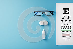 Glasses with Contact Lenses, drops and an Optometrist`s Eye Test Chart On a Blue Background