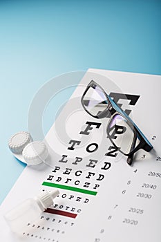 Glasses with Contact Lenses, drops and an Optometrist`s Eye Test Chart On a Blue Background