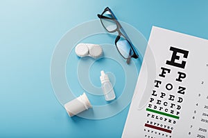 Glasses with Contact Lenses, drops and an Optometrist`s Eye Test Chart On a Blue Background