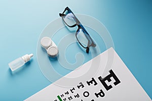Glasses with Contact Lenses, drops and an Optometrist`s Eye Test Chart On a Blue Background