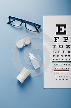 Glasses with Contact Lenses, drops and an Optometrist`s Eye Test Chart On a Blue Background