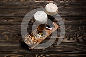 Glasses of dark and light beer near bowl with roasted peanuts on wooden table.