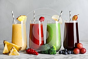 Glasses of delicious juices and fresh ingredients on white marble table