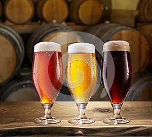 Glasses of different chilled beer and wooden beer casks on the background