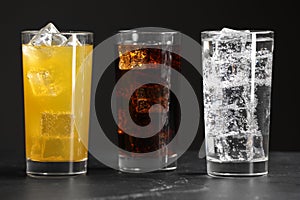 Glasses of different refreshing soda water with ice cubes on grey table