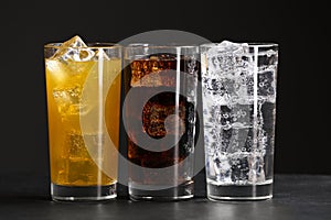 Glasses of different refreshing soda water with ice cubes on grey table