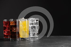 Glasses of different refreshing soda water with ice cubes on grey table, space for text