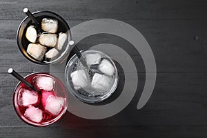 Glasses of different refreshing soda water with ice cubes and straws on black table, flat lay. Space for text