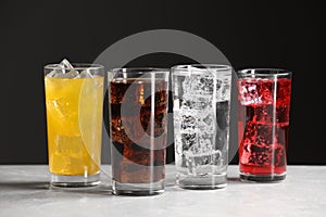 Glasses of different refreshing soda water with ice cubes on white marble table