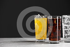 Glasses of different refreshing soda water with ice cubes on white marble table, space for text