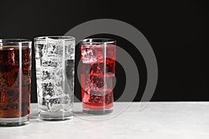 Glasses of different refreshing soda water with ice cubes on white marble table, space for text