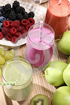 Glasses of different tasty smoothies and fresh ingredients on wooden table, above view