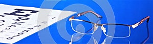 Glasses with diopters and visual acuity test table. Glasses - optical device for vision correction. Table with symbols to check