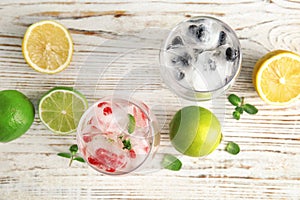 Glasses of drinks with ice cubes and fruits on wooden background