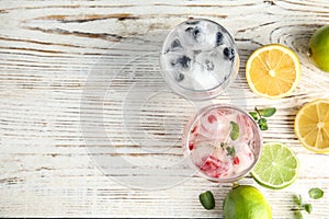 Glasses of drinks with ice cubes and fruits on wooden background, flat lay.