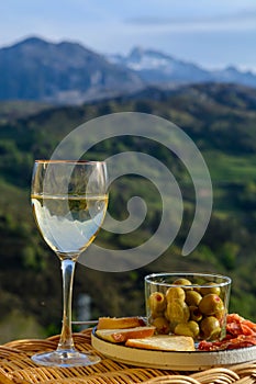 Glasses of dry white wine and spanish tapas olives in bowl with mountains peaks on background in sunny day photo