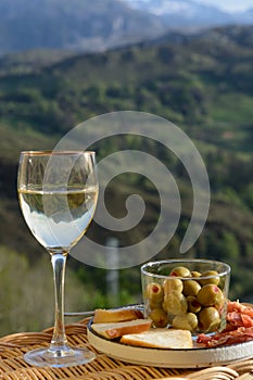 Glasses of dry white wine and spanish tapas olives in bowl with mountains peaks on background in sunny day photo