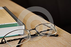 Glasses on the edge of the table next to the book close up with copy space