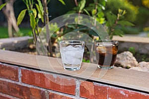 2 glasses filled with ice, 1 with water and 1 with soft drink, on a brick wallflower outdoors on a summer afternoon. photo