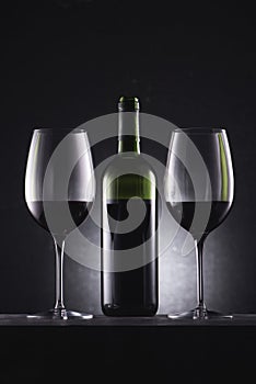 glasses filled with red wine and wine bottle in middle