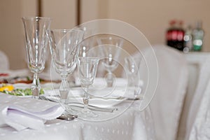 Glasses, flowers, fork, knife, napkin folded in a pyramid, served for dinner in restaurant with cozy interior. Wedding decorations