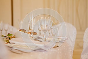 Glasses, flowers, fork, knife, napkin folded in a pyramid, served for dinner in restaurant with cozy interior. Wedding decorations