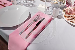 Glasses, forks, knives, napkins and a decorative flower on a white tablecloth table are served for dinner in a cozy restaurant. De