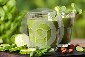 Glasses of fresh green smoothie and ingredients on wooden table, closeup