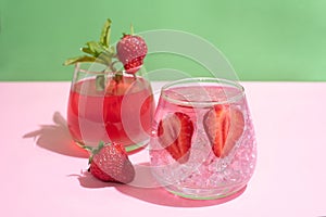 Glasses with functional water, strawberry lemonade with ice cubes on green and pink background, summer drinks concept
