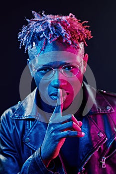 In glasses. Futuristic neon lighting. Young african american man in the studio