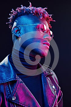 In glasses. Futuristic neon lighting. Young african american man in the studio