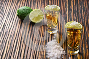 Glasses gold tequila with green lime on a wooden background ,se