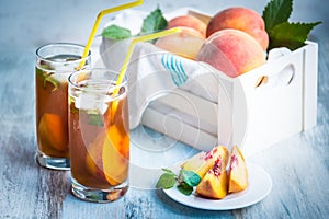 Glasses with homemade ice tea, peach flavored. Freshly cut peach slices for arrangement. White crate full with peaches in the back