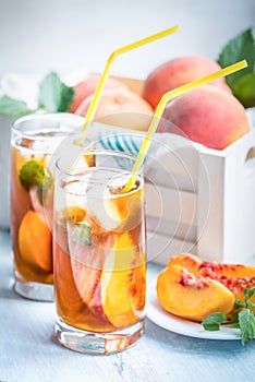 Glasses with homemade ice tea, peach flavored. Freshly cut peach slices for arrangement. White crate full with peaches in the back