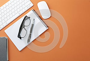 Glasses keyboard mouse pen notepad and diary on orange background