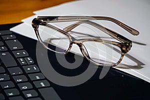 Glasses laptop keyboard and notes on wooden background business concept close up view