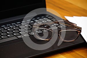 Glasses laptop keyboard and notes on wooden background business concept close up view