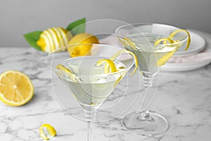 Glasses of lemon drop martini  with zest on marble table against grey background