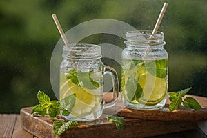 Glasses with lemon water and mint, mojito drink, on a wooden board, outdoors