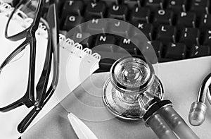 glasses, a medical stethoscope on a computer keyboard and a ballpoint pen for notes
