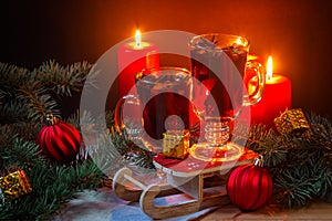 Glasses of mulled wine, burning candles, christmas balls, pine branches and gifts on wooden table. Selective focus