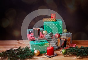 Glasses of mulled wine, colorful gifts, christmas balls, fir branches and burning candle on dark background. Selective focus