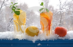 Glasses with natural lemon and tangerine drink with mint in the snow