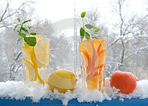 Glasses with natural lemon and tangerine drink with mint in the snow